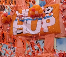 Foto van de gevel van een Nederlandse huis; de gevel is versierd met oranje spullen; de foto zal genomen zijn tijdens een groot internationaal voetbaltoernooi waaraan het Nederlands voetbalelftal deelnam. Onderschrift foto: 'Oranje: het begon allemaal met een sinaasappel. (Fotobron: flickr.com)'