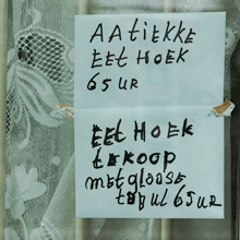 Foto van een briefje op een raam; op het briefje staat: “aatiekke eet hoek 65 ur - eet hoek te koop met glaase taful 65 ur”